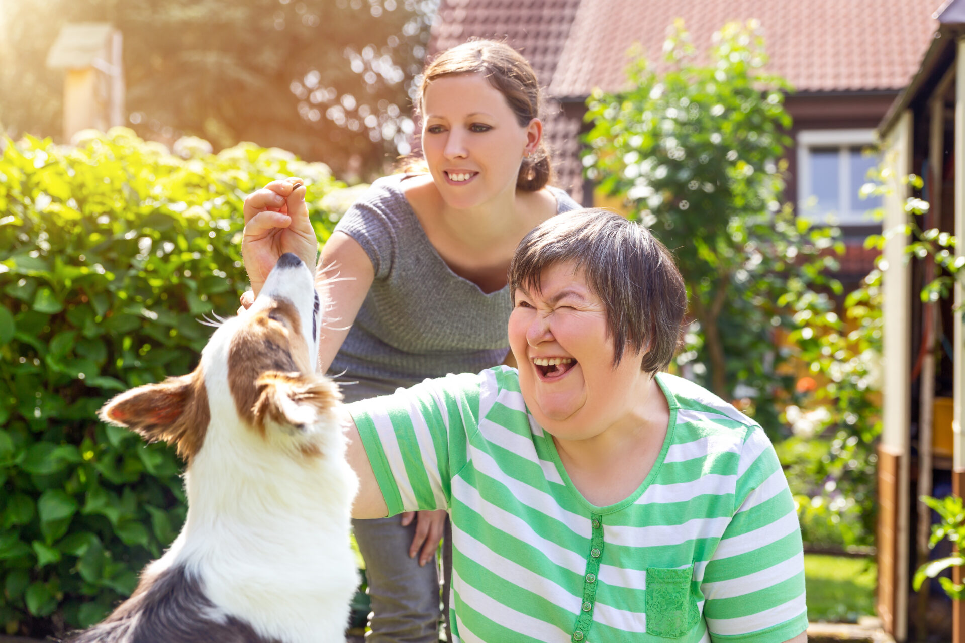 EIne Frau mit Down-Syndrom und ihre Therapeutin füttern einen Hund.