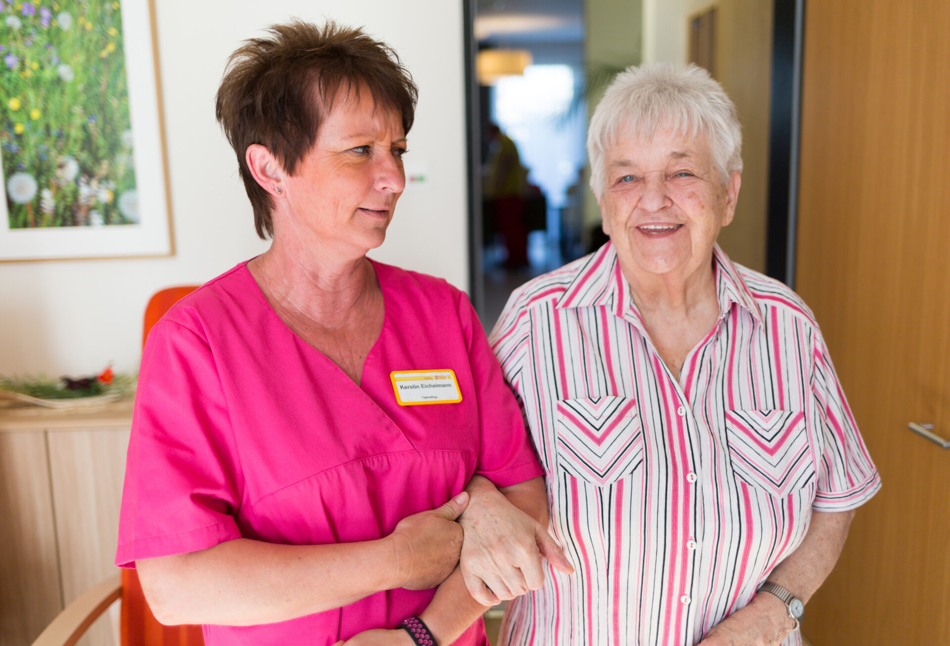 Eine Pflegekraft begleitet eine Seniorin durch ein Pflegeheim.