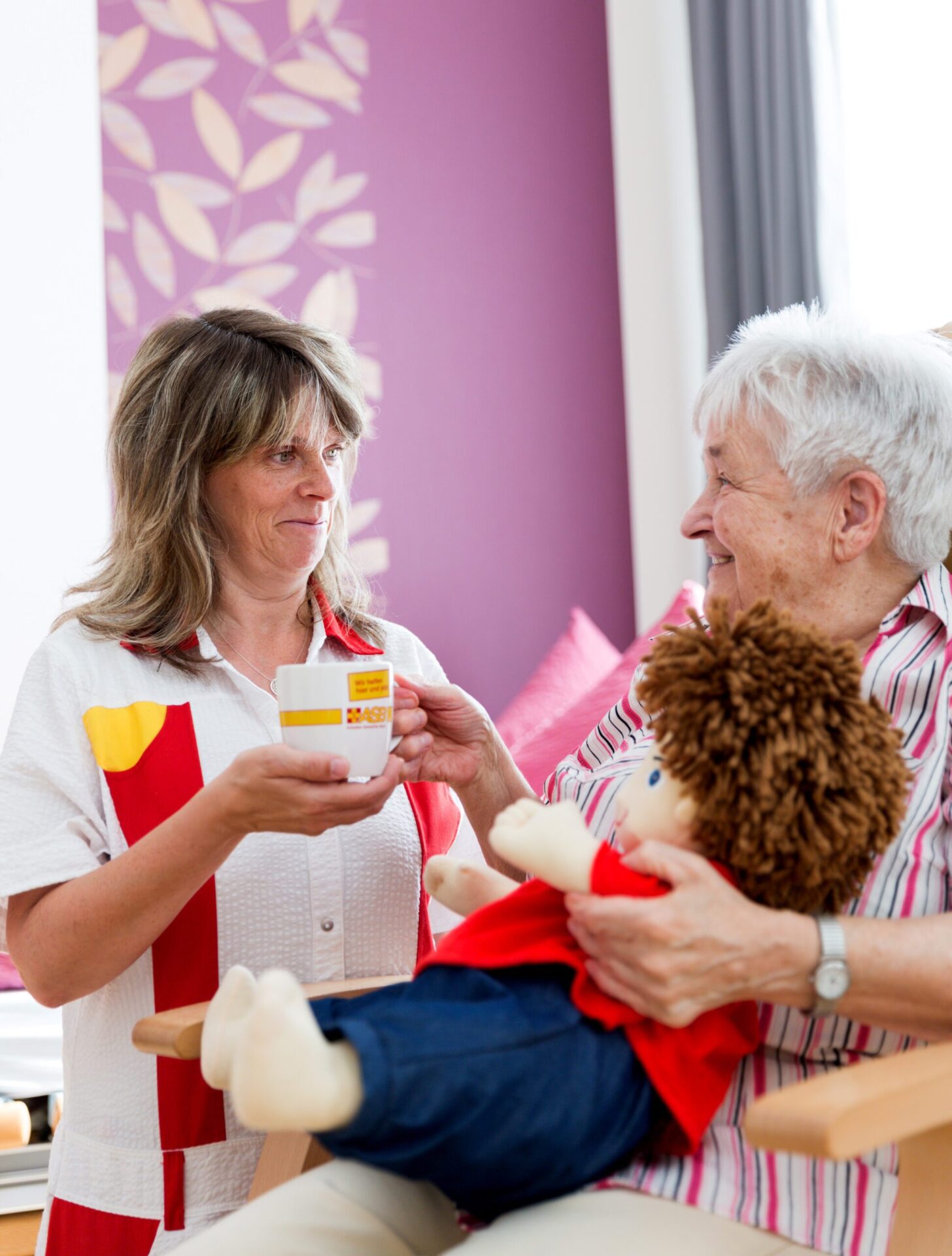 Eine Pflegekraft reicht einer Seniorin eine Tasse Tee.