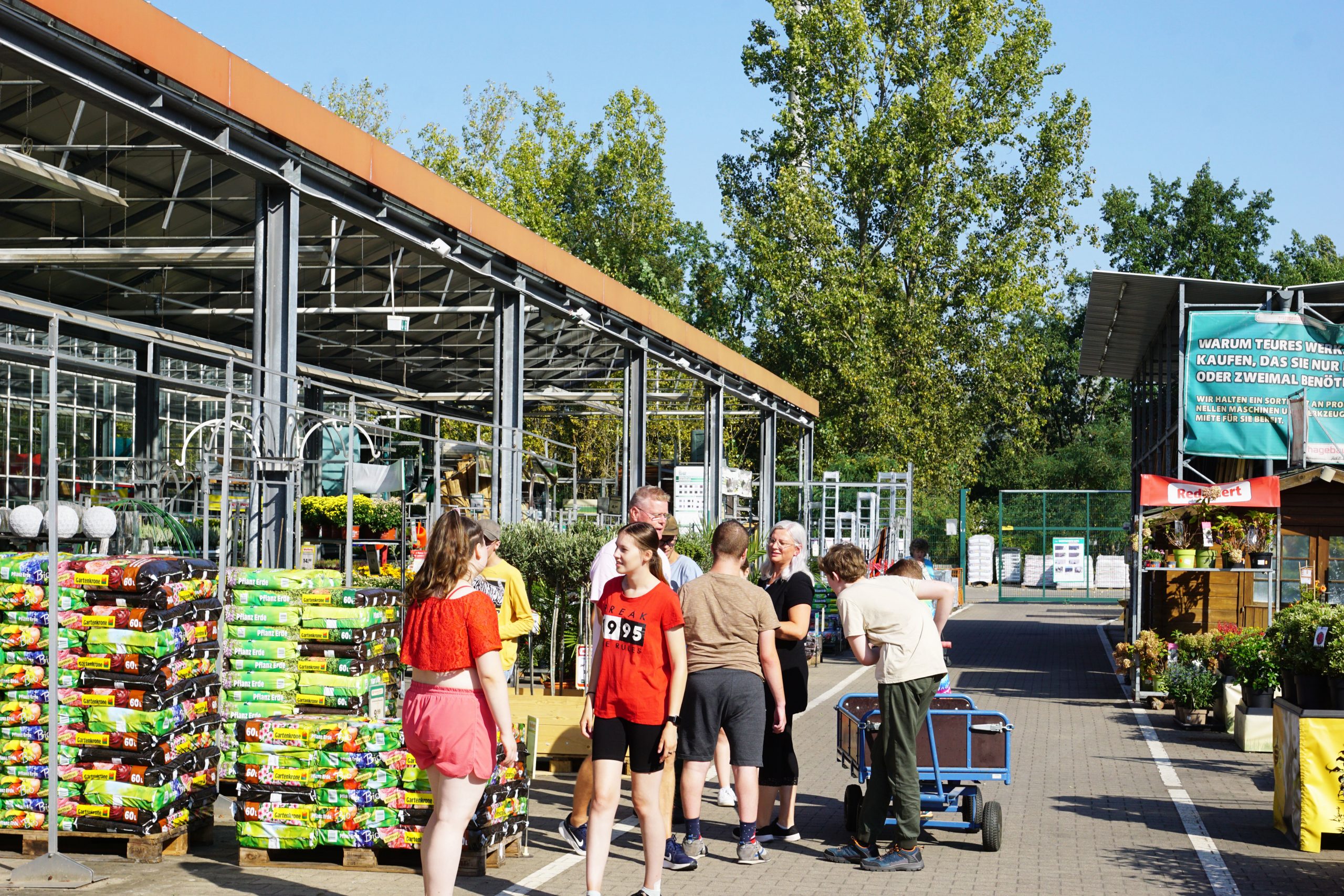 Eine Gruppe junger Menschen steht mit zwei Betreuern in einem Baumarkt in der Pflanzenabteilung.
