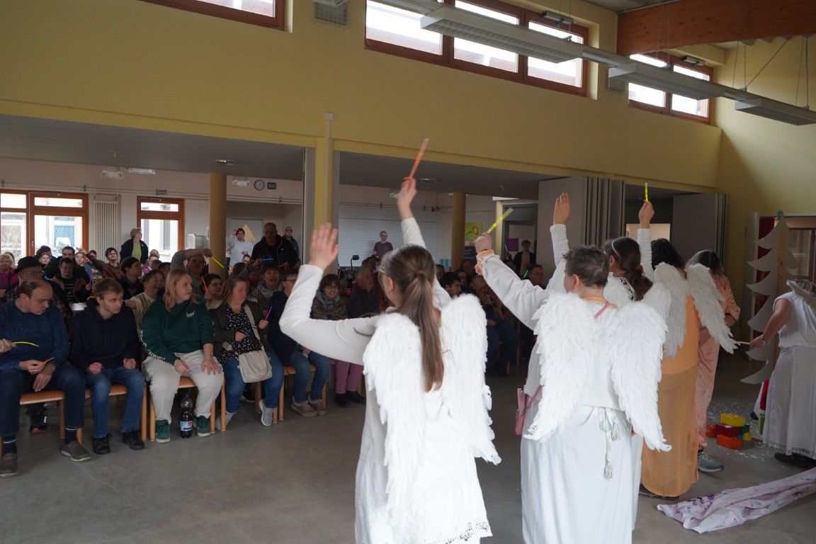 Eine Gruppe junger Menschen stehen als Engel verkleidet vor einem Publikum und spielen ein Theaterstück vor.