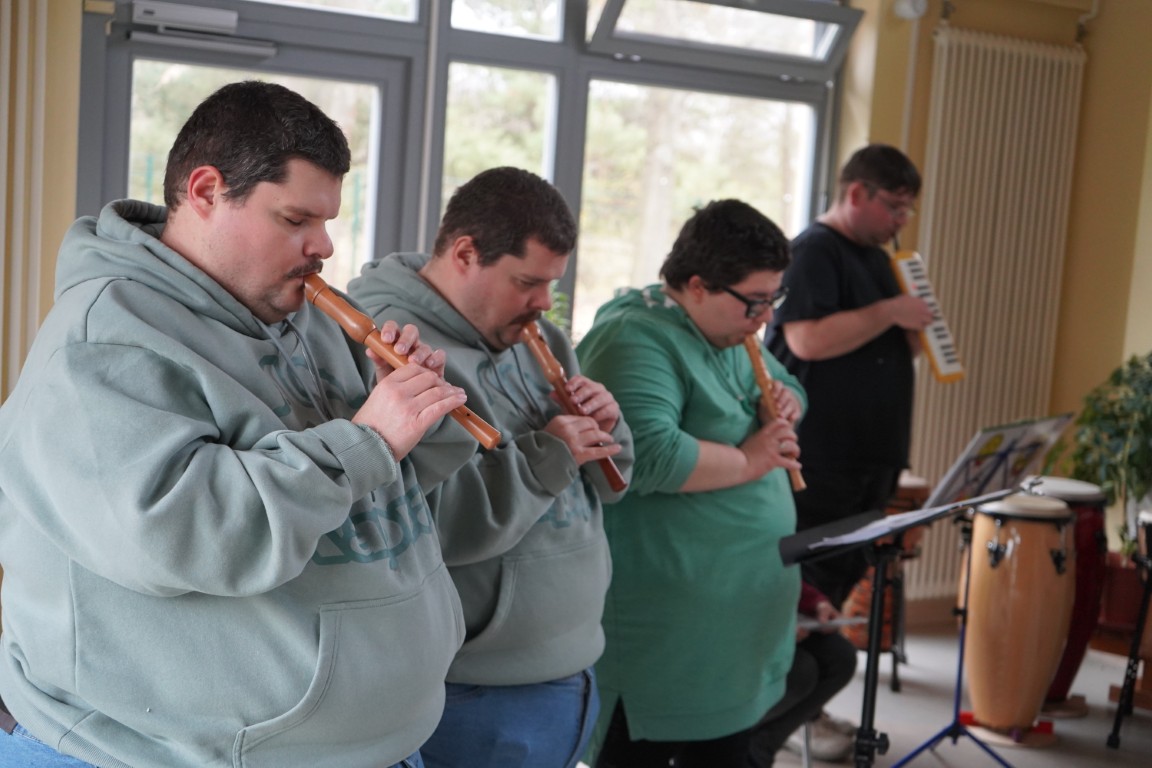 Vier junge Menschen stehen in einer Reihe vor einem Notenständer und spielen jeweils die Blockflöte.
