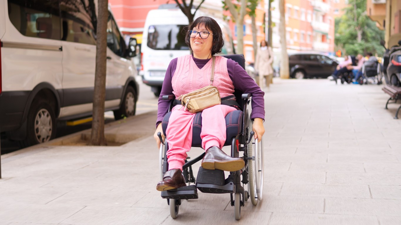 Eine junge Frau sitzt in einem Rollstuhl und bewegt sich durch die Stadt und lächelt.