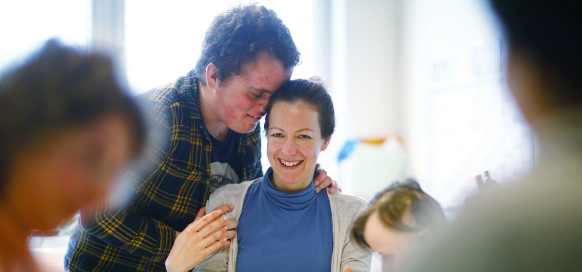 Ein junger Mensch mit Behinderung umarmt eine junge Frau
